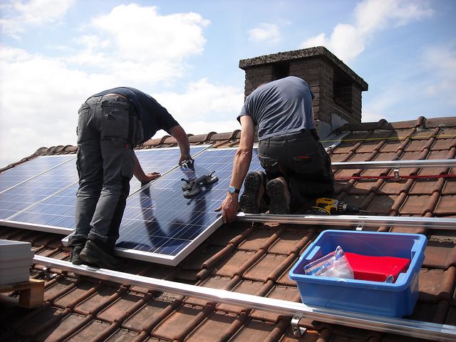 Two workers installing commercial solar panels in the roof